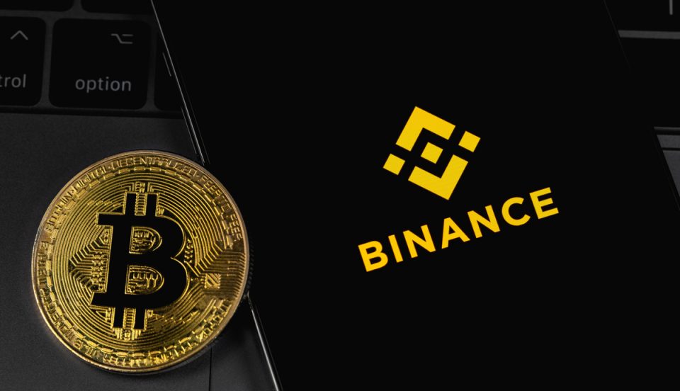 Logo da Binance na tela do smartphone com bitcoin ao lado